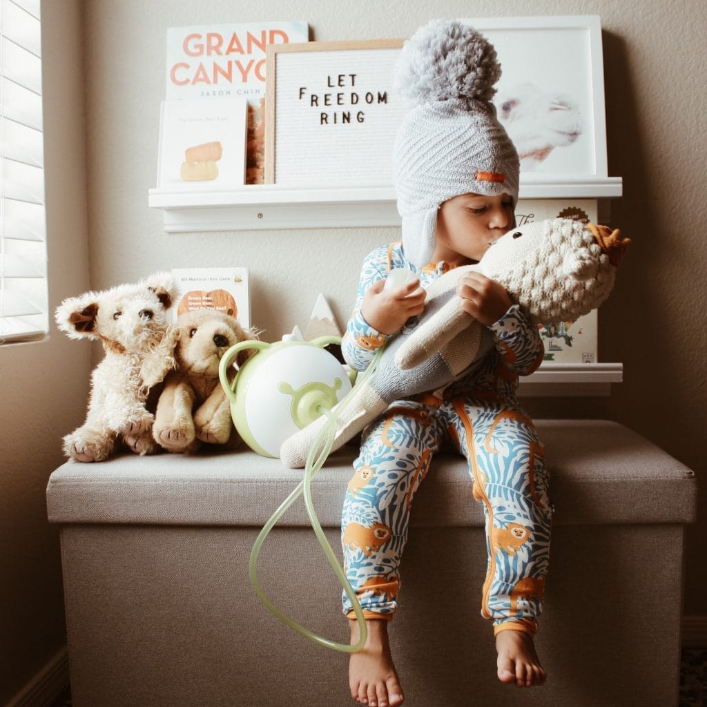 Little boy is sitting next to the Nosiboo Pro nasal aspirator and kissis his favourite plush toy